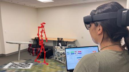 A researcher holding a laptop and wearing a augmented reality glasses as part of research on Parkinson's.